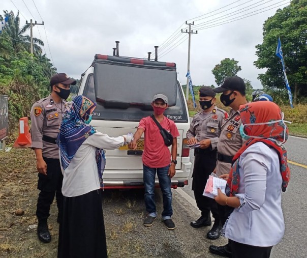 Personel Polsek Bandar Sei Kijang membagikan masker kain secara gratis kepada masyarakat yang melintas di Jalan Lintas Timur, tepatnya di depan Pos Operasi Lilin, Sabtu (2/1/2021). Foto: Istimewa. 